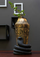 a hand embossed brass vase is kept in a hand carved black stone snake shaped holder, a plant is decorated in it