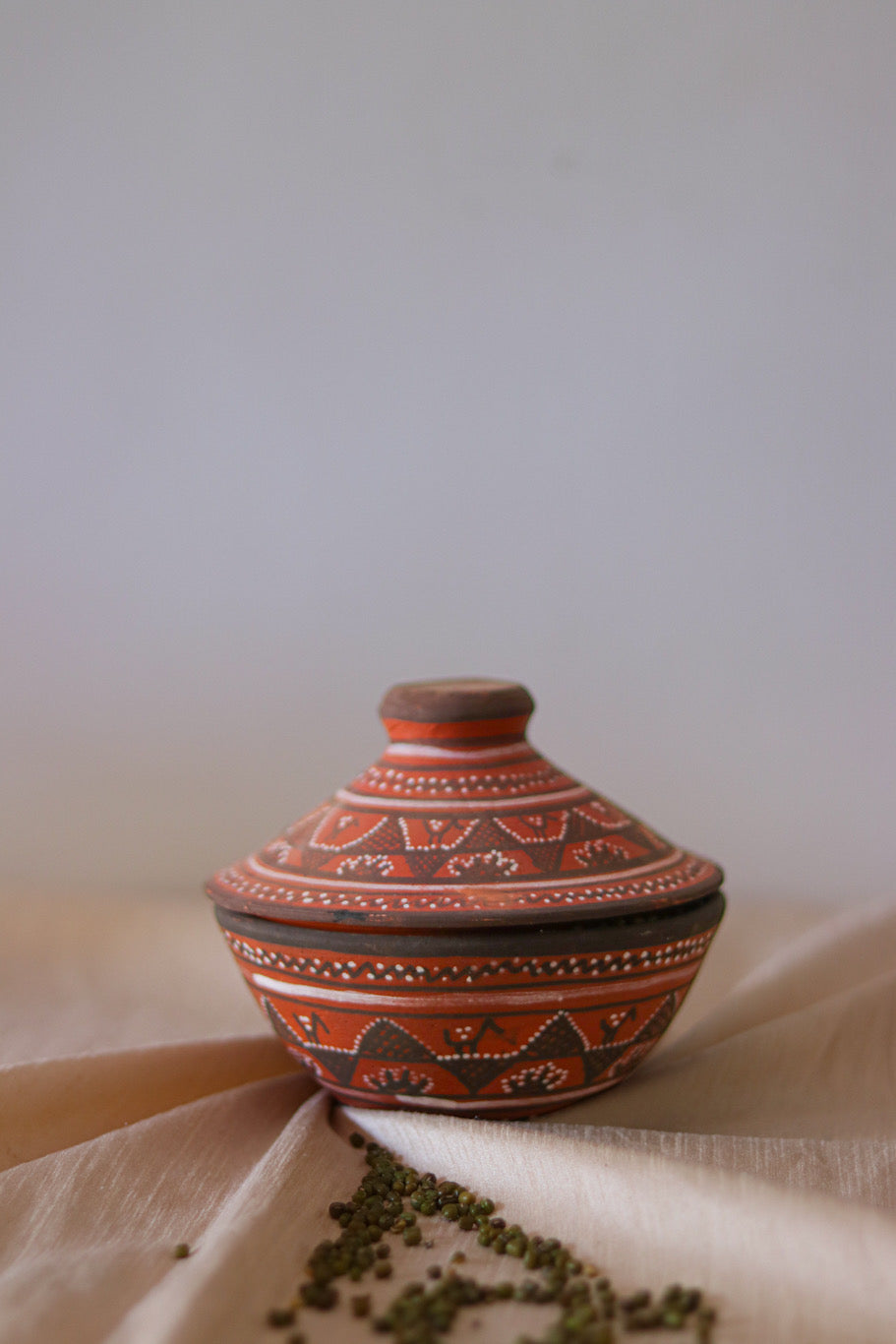 a red hand painted pottery serving bowl with hand painted lid is sitting on top of a white cloth