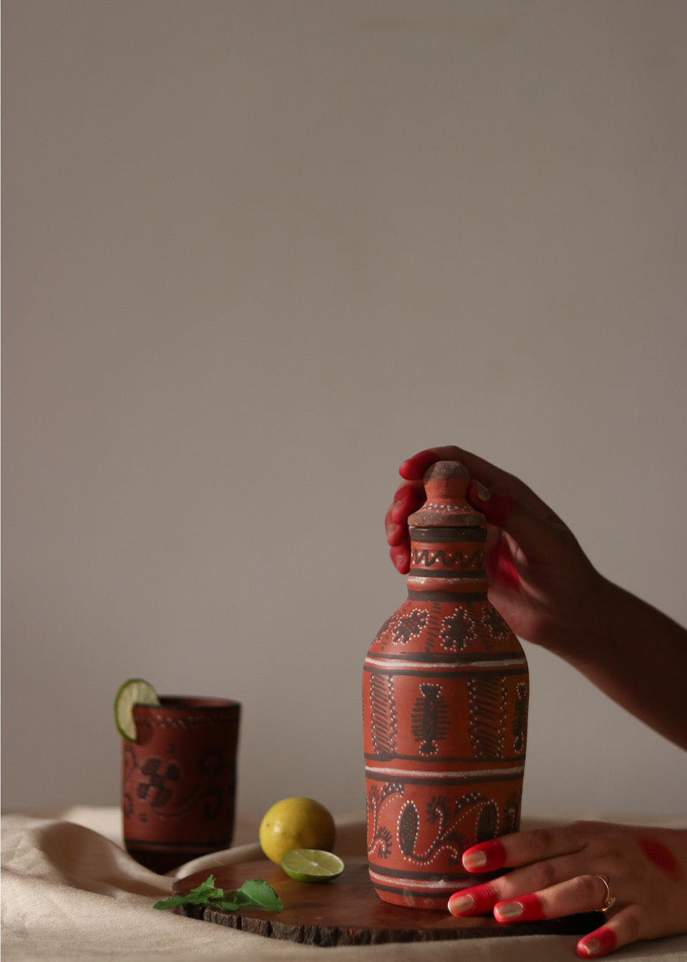 Red clay hand painted water bottle is kept on the table along with red clay hand painted glass