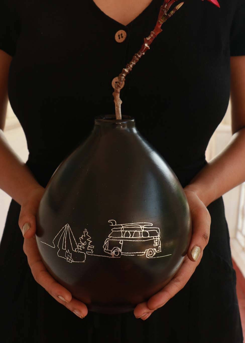 a woman holding black clay vase with silver inlay motifs