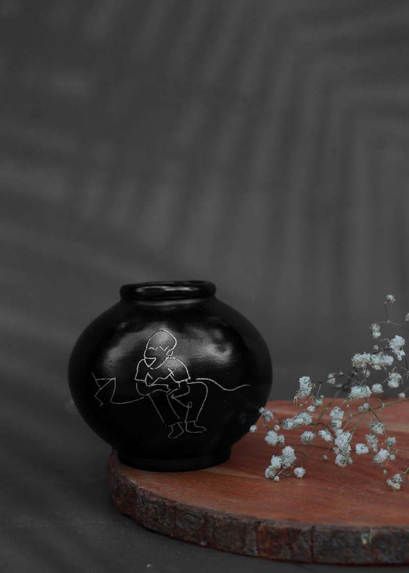 A round black clay vases with silver inlay motifs is decorated with purple flower is kept on the table