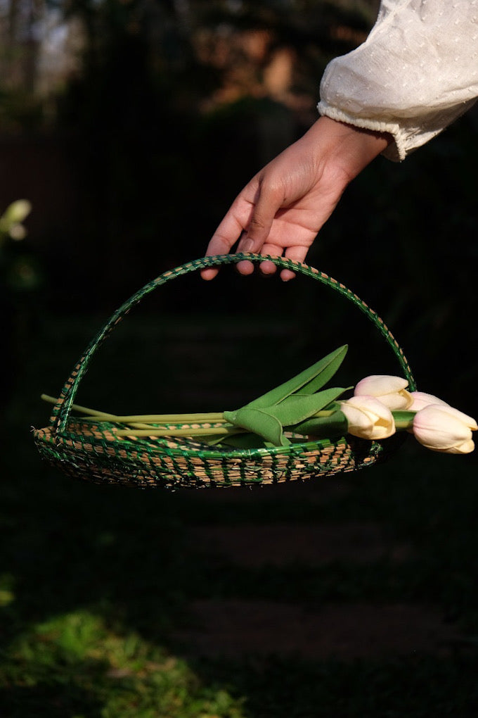 a girl is holding Green coloured sikki flower basket is decorated with flower 