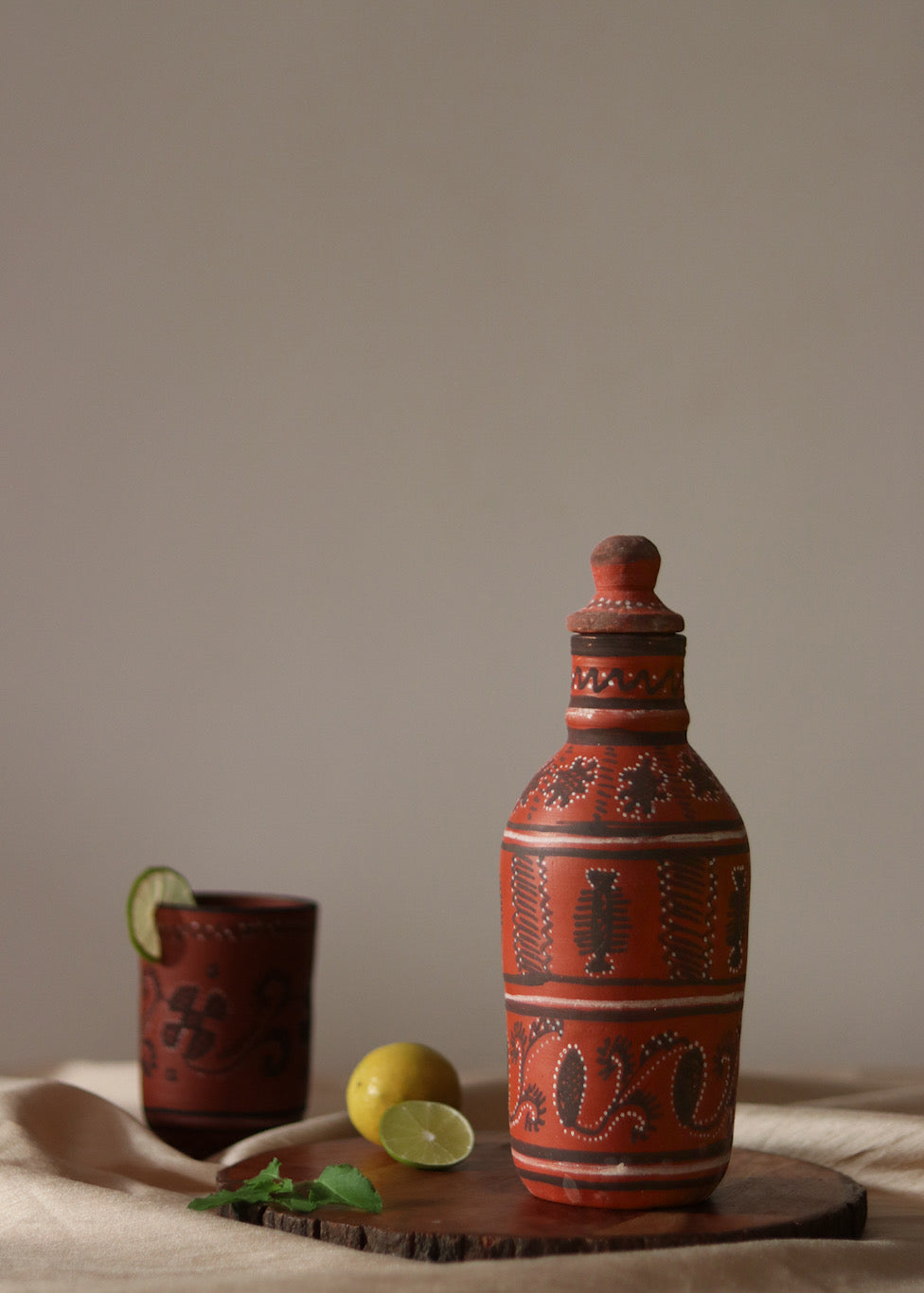 Red clay hand painted water bottle is kept on the table along with red clay hand painted glass