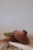 a red hand painted pottery serving bowl with hand painted lid kept on the side