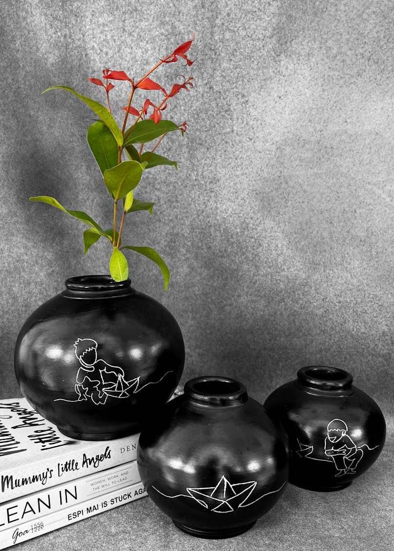 a set of three round black clay vases with silver inlay motifs are kept on the table