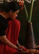 a woman sitting next to a copper embossed vase decorated with flower kept on a table