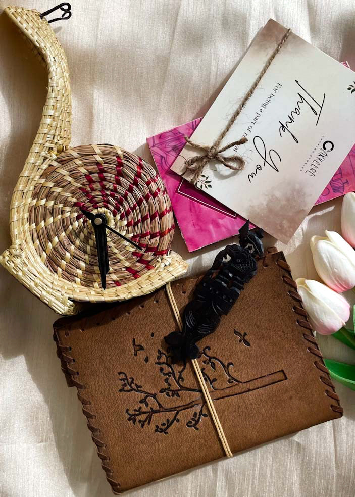 Sikki woven snail table clock is kept along with leather diary and rosewood bookmark and personalised card on a white sheet 