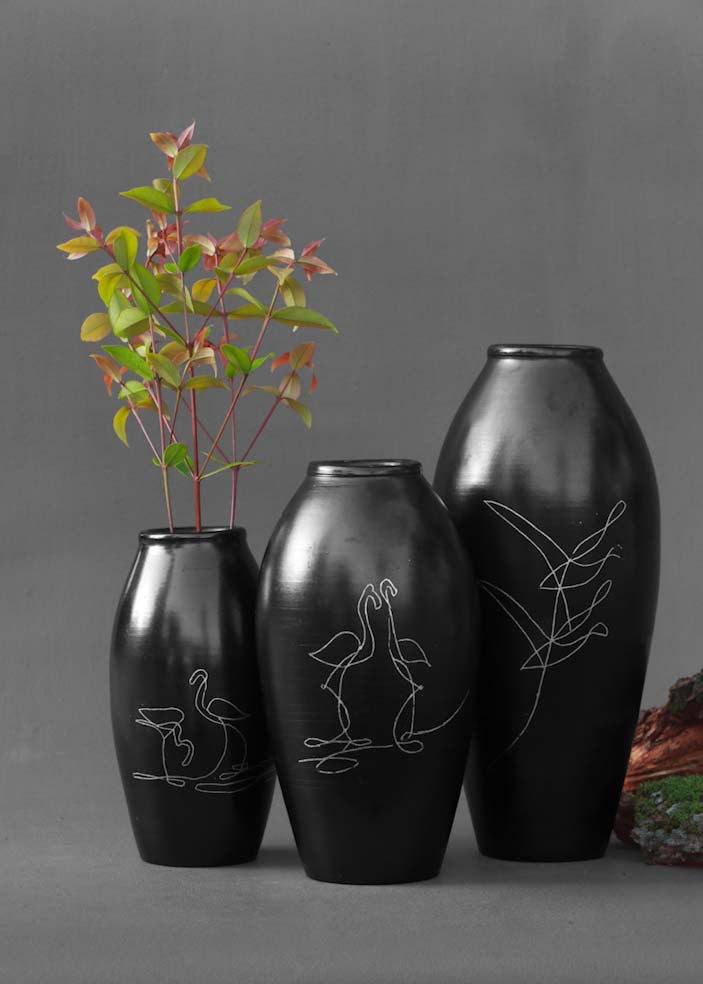 a set of three black clay vases with silver inlay motifs are kept on the table