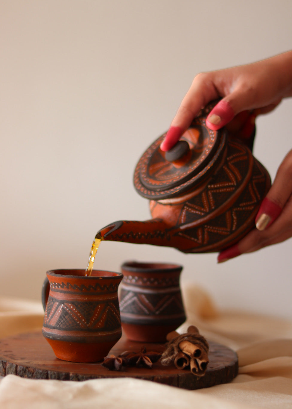 Red clay hand painted tea cups kept on the table with red hand painted tea pot pouring tea