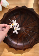 dark brown hand carved rosewood plate is kept on the table with flowers kept in it