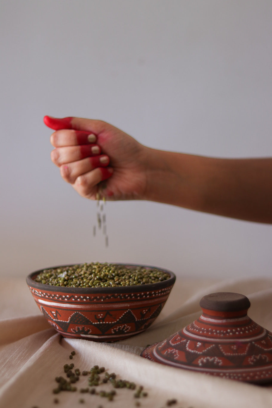 a woman is sprinkling seeds into a a red hand painted pottery serving bowl