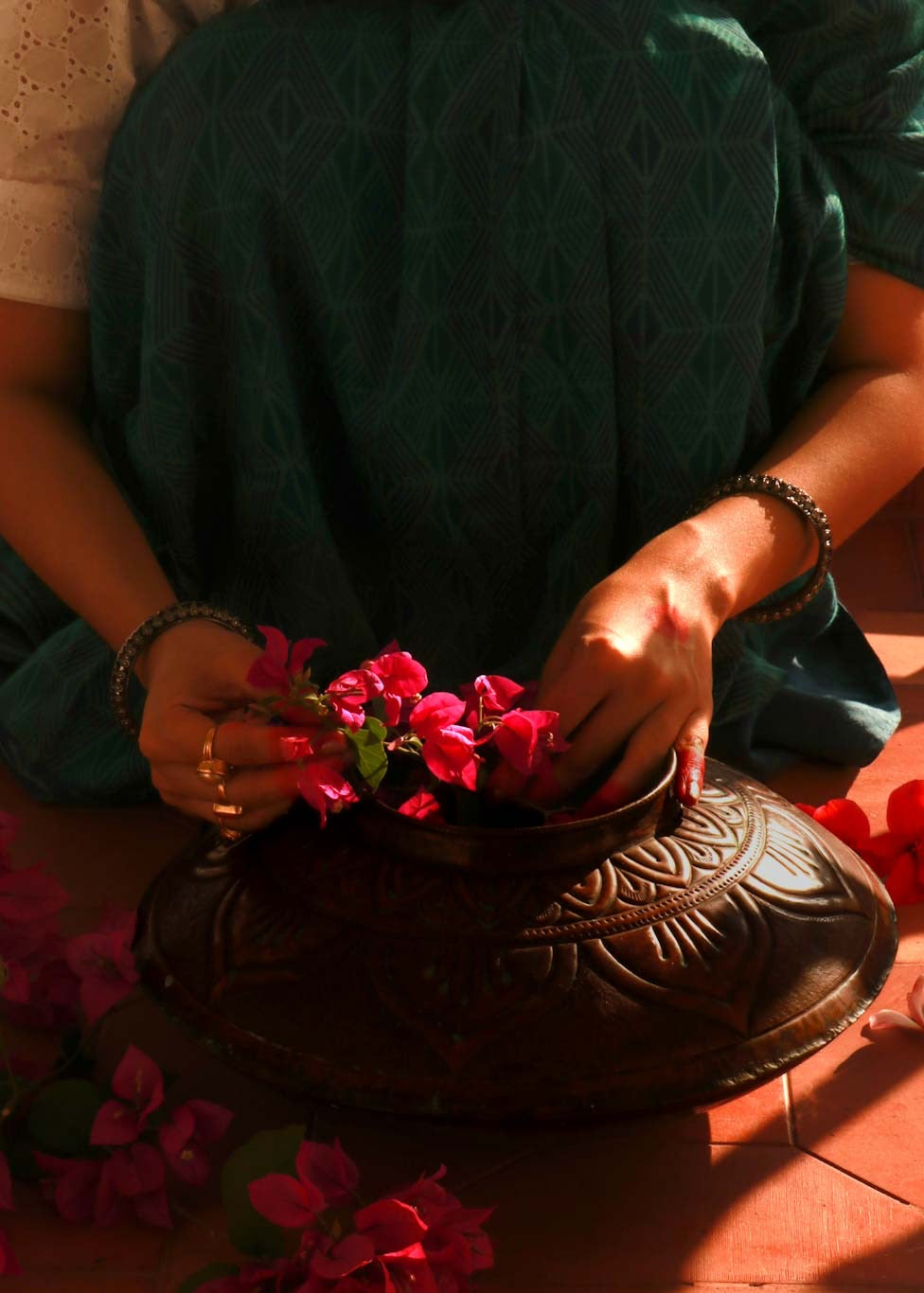 Copper embossed Vase kept on floor while a woman decorates it with flower