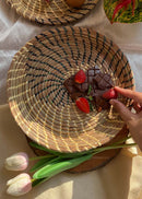 hand woven sikki plate with swirl pattern in blue is kept on the table, strawberries and chocolates are kept on it