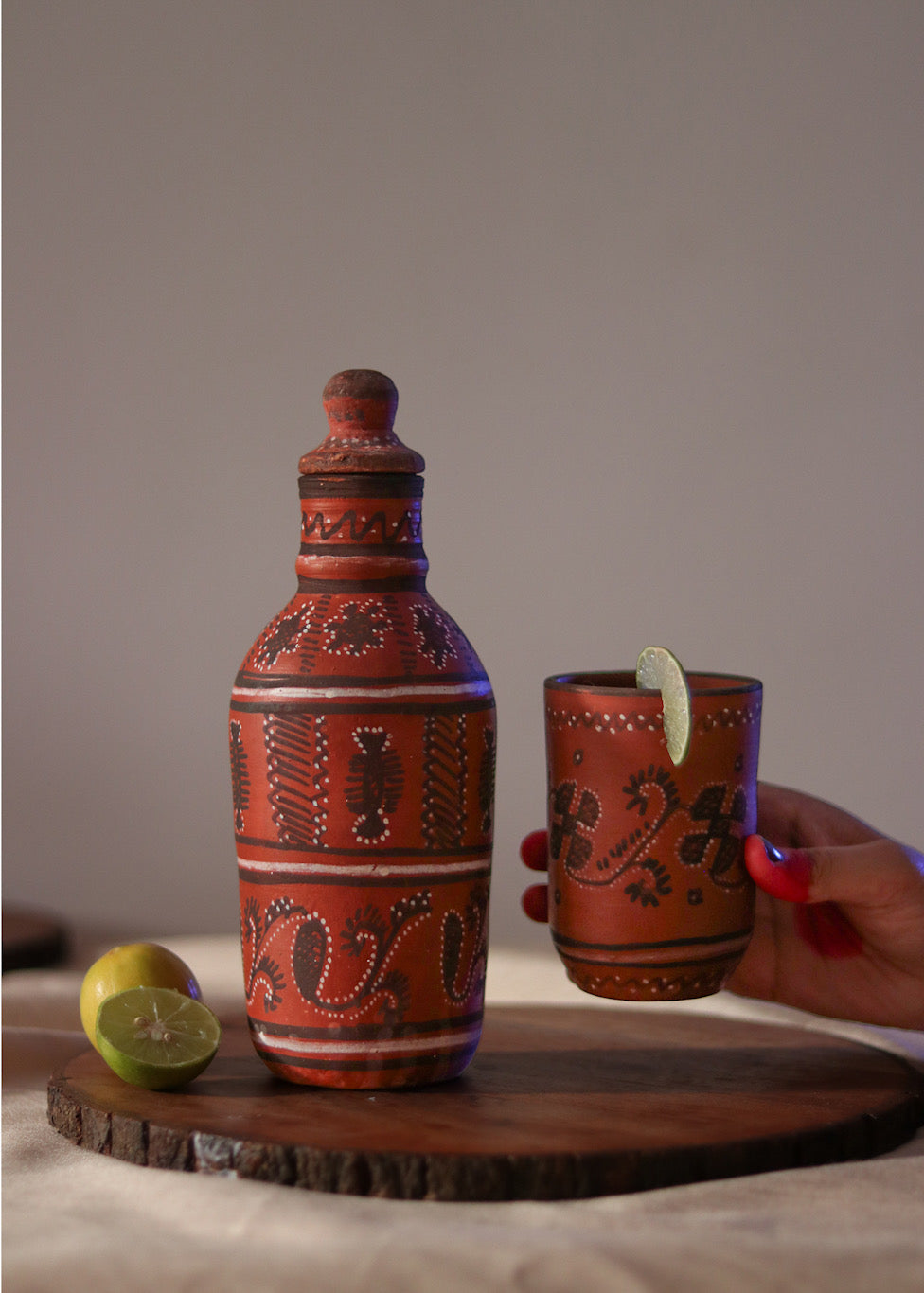 Red clay hand painted water bottle is kept on the table and red clay hand painted glass is being picked by a woman