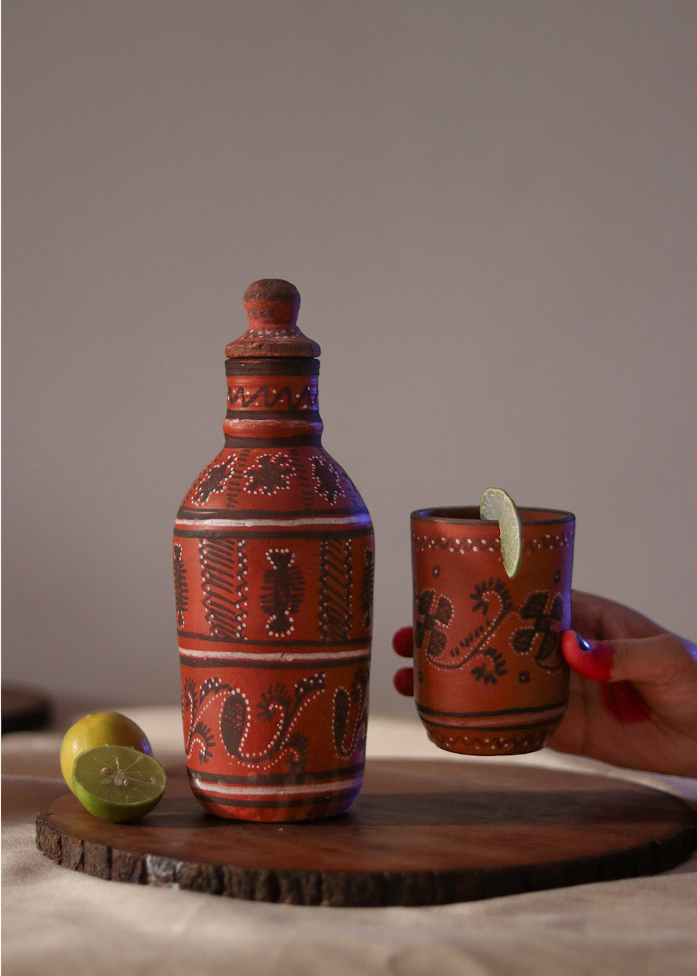 Red clay hand painted water bottle is kept on the table  and red clay hand painted glass is being picked by a woman