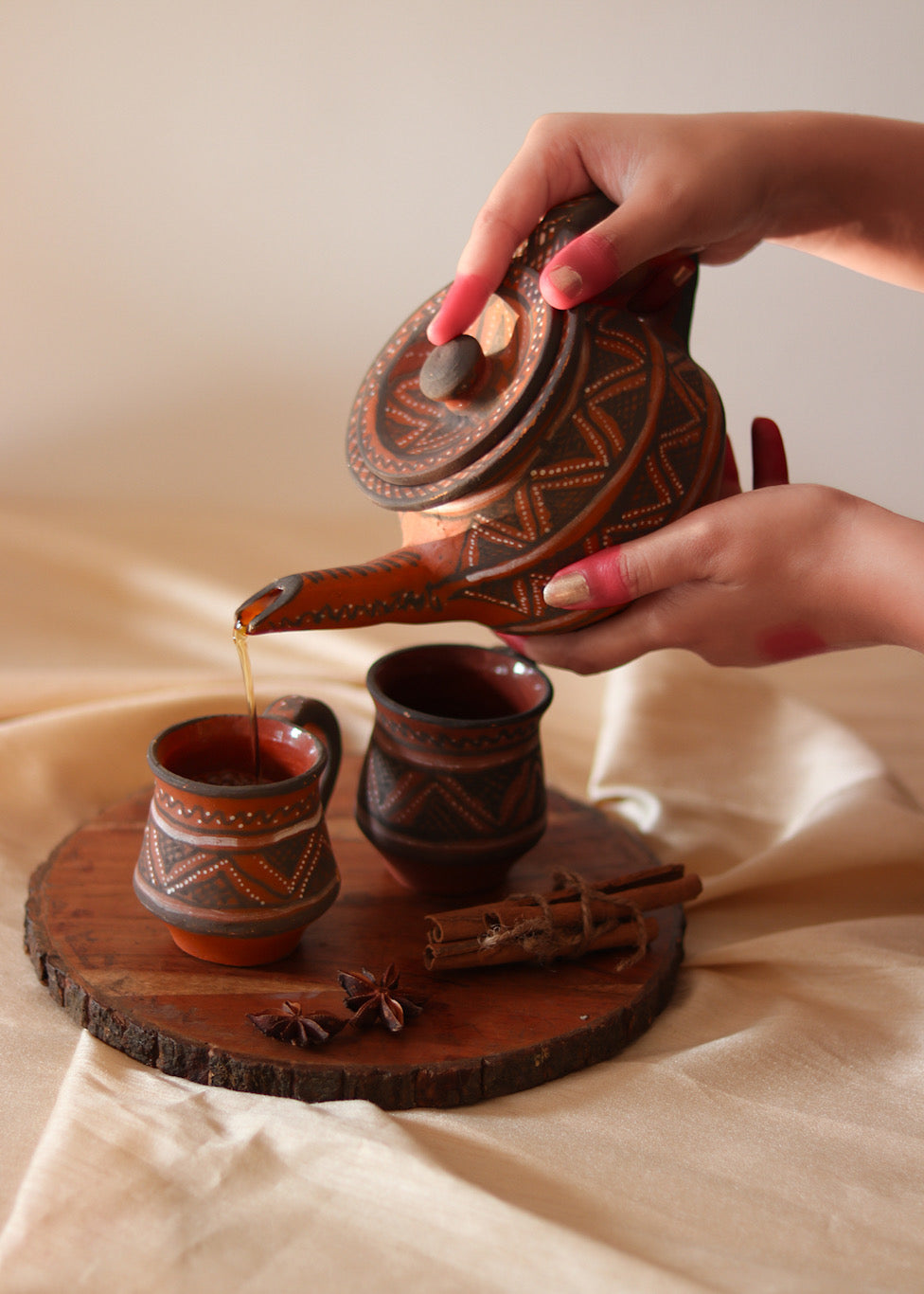 Red clay hand painted tea cups kept on the table with red hand painted tea pot pouring tea