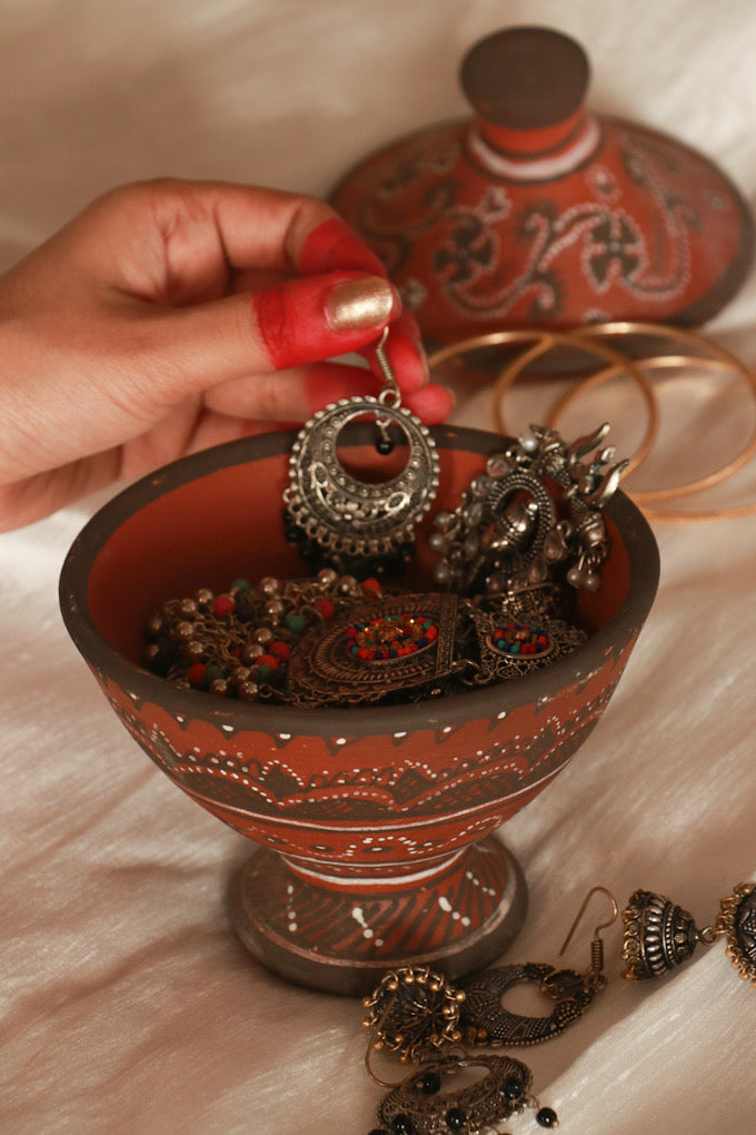 A woman  keeping her earrings  in red pottery hand painted khavda jewellery keeper