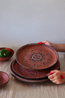 A red hand painted dinner set is kept on the table and a hand is picking it up one by one