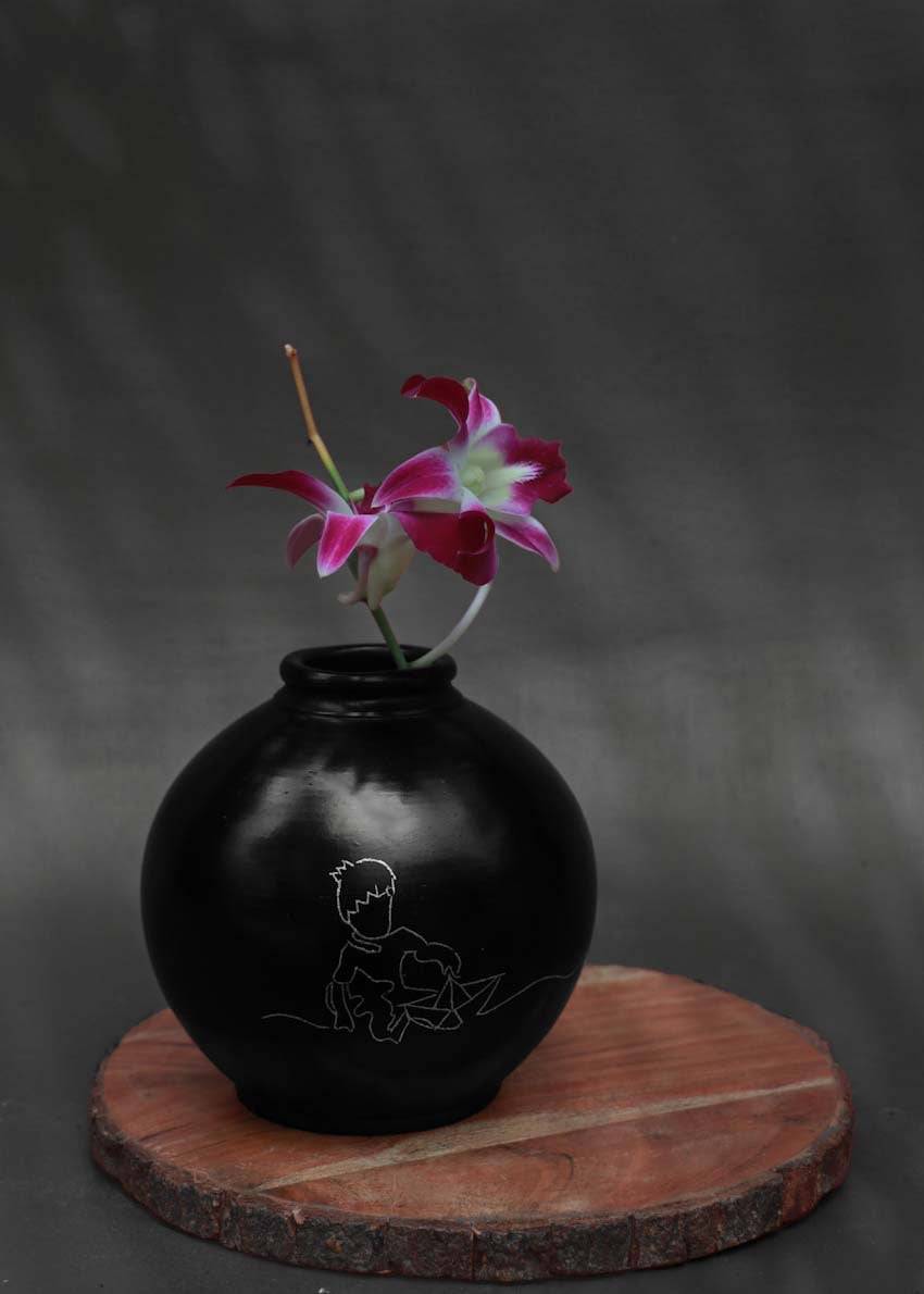 A round black clay vases with silver inlay motifs is decorated with purple flower is kept on the table