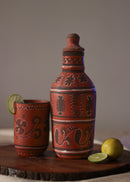 Red clay hand painted water bottle is kept on the table along with red clay hand painted glass