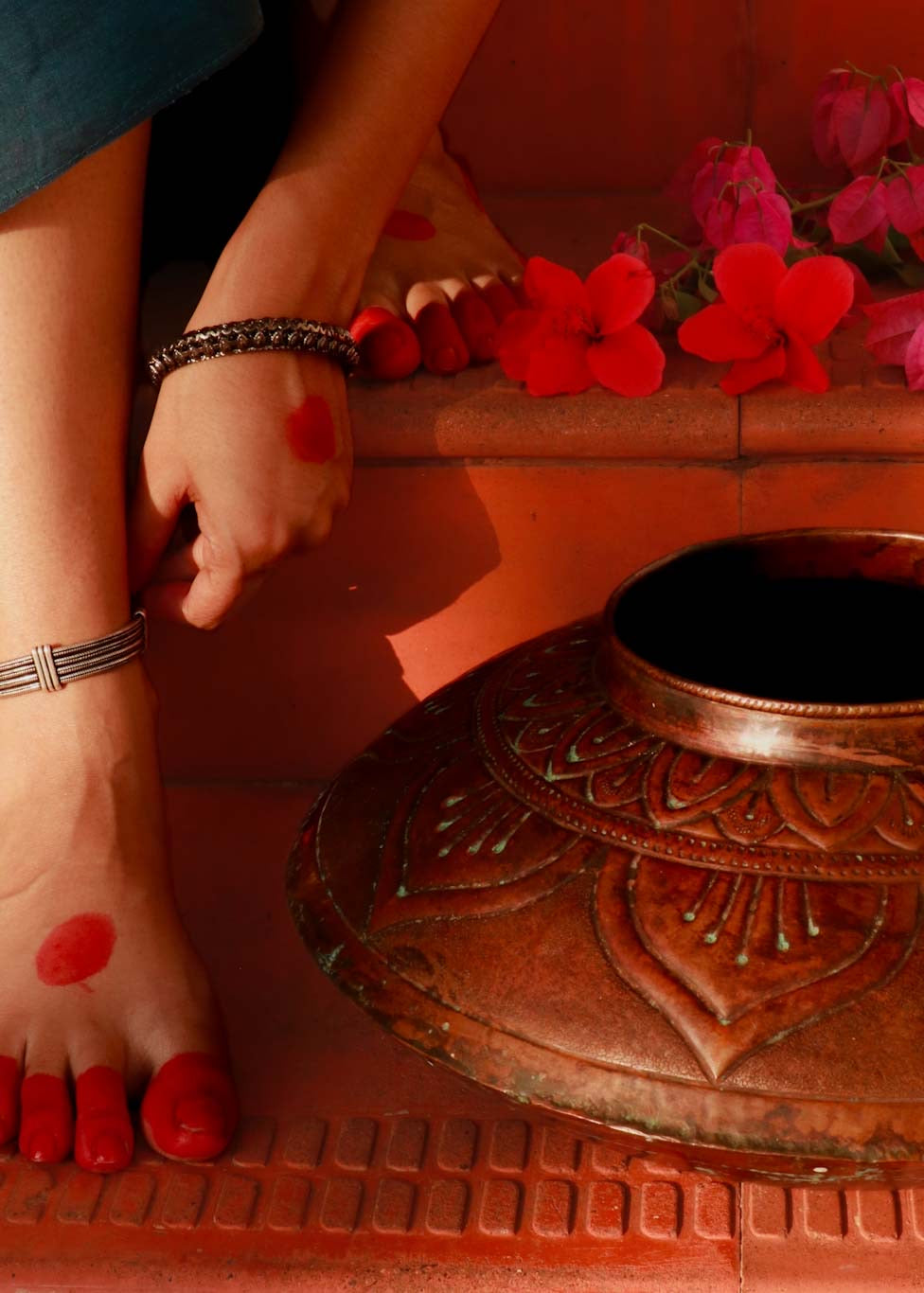 Copper embossed Vase kept on floor next to a women adoring jewellery