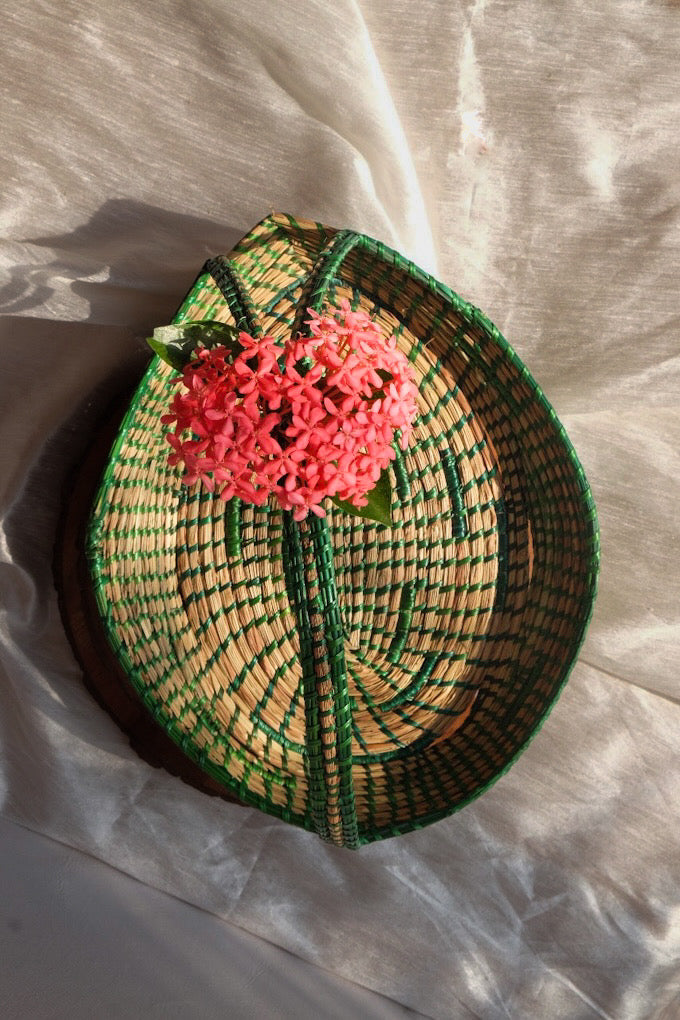 Green coloured sikki flower basket is decorated with flower and is kept on table