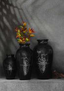 a set of three black clay vases with silver inlay motifs are kept on the table