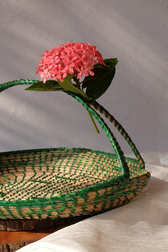 Green coloured sikki flower basket is decorated with flower and is kept on table