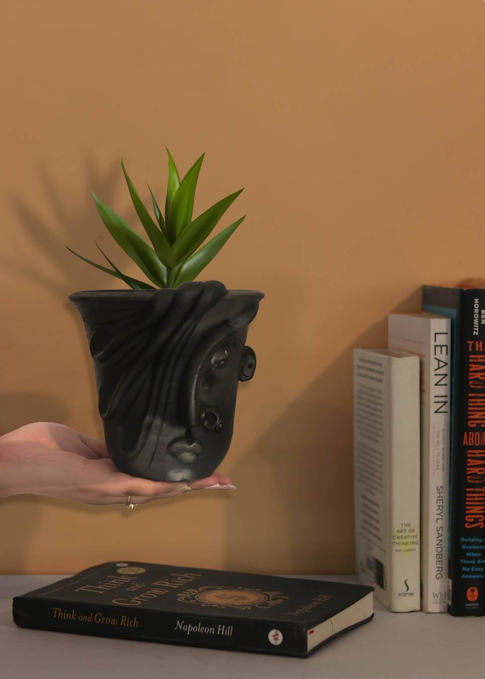 a woman shaped black planter is held in the hand of a woman