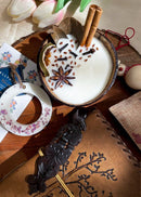 a hand poured coconut candle decorated with spices, a rosewood bookmark, a leather diary and a wax tag kept on a table