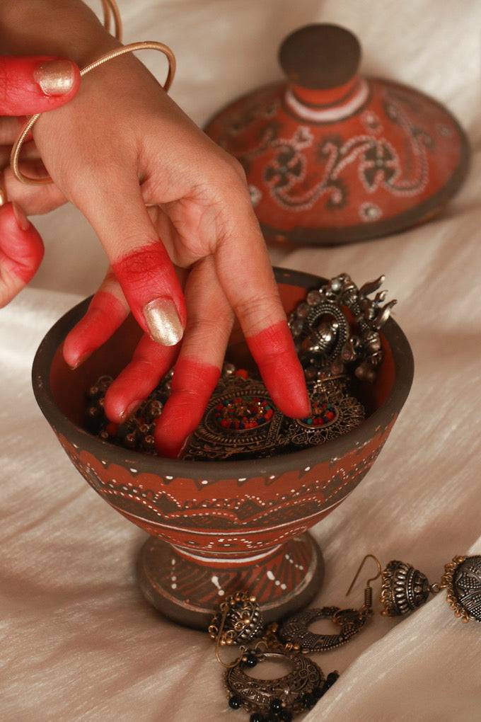 A woman taking out her bangles and keeping it in red pottery hand painted khavda jewellery keeper