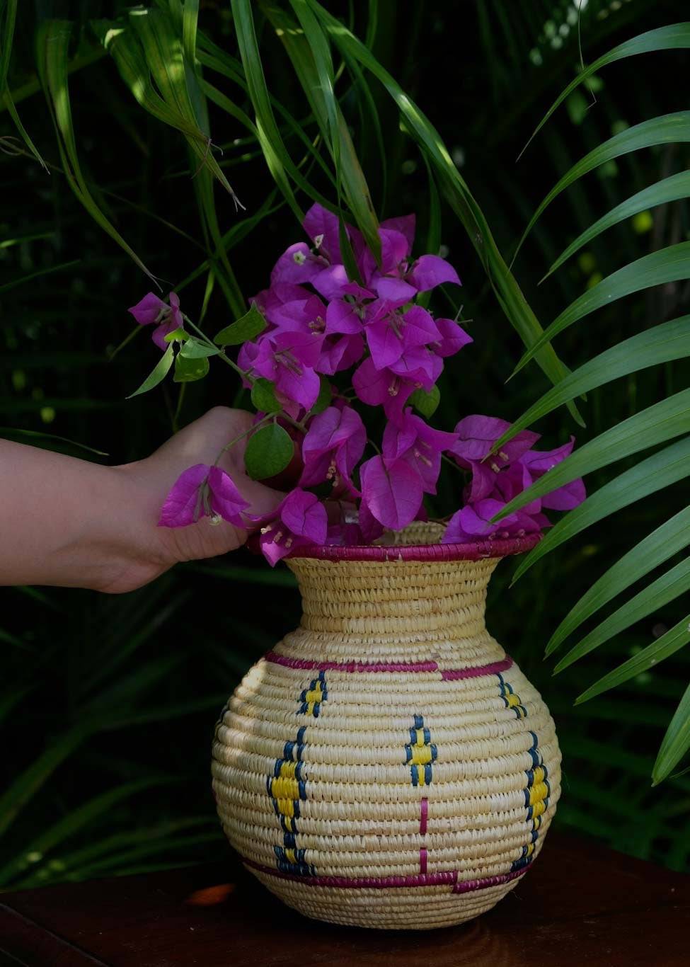 a girl is decorating flower in Sikki grass vase that is kept on a table in a garden