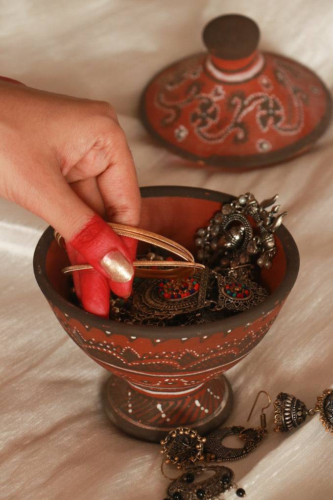 A woman taking out her bangles and keeping it in red pottery hand painted khavda jewellery keeper